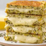 Stack of zucchini grilled cheese sandwiches with melted cheese oozing out.