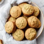 Freshly baked zucchini muffins in a bowl lined with a striped cloth.