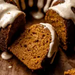 A moist slice of pumpkin bundt cake with creamy glaze, served on a wooden surface.