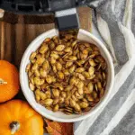 A bowl of crispy air fryer pumpkin seeds seasoned with spices, surrounded by mini pumpkins and autumn decor.