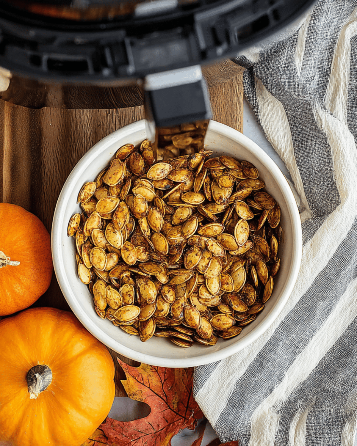 A bowl of crispy air fryer pumpkin seeds seasoned with spices, surrounded by mini pumpkins and autumn decor.