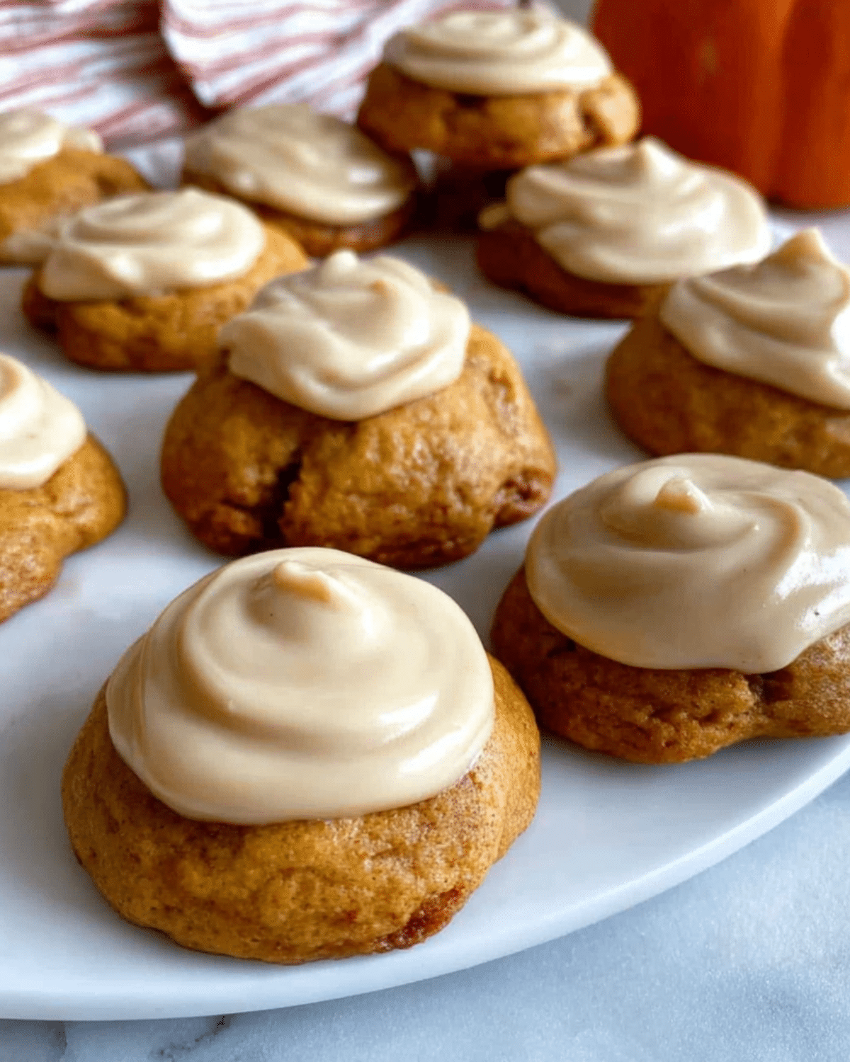 Soft Amish pumpkin cookies with frosting neatly arranged on a white plate.
