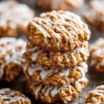 Stack of apple cinnamon oatmeal cookies drizzled with white icing, placed on a cooling rack with more cookies in the background.