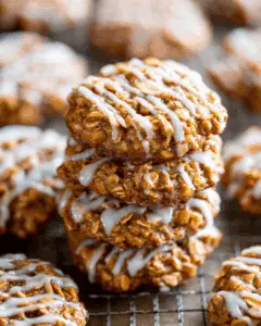 Stack of apple cinnamon oatmeal cookies drizzled with white icing, placed on a cooling rack with more cookies in the background.