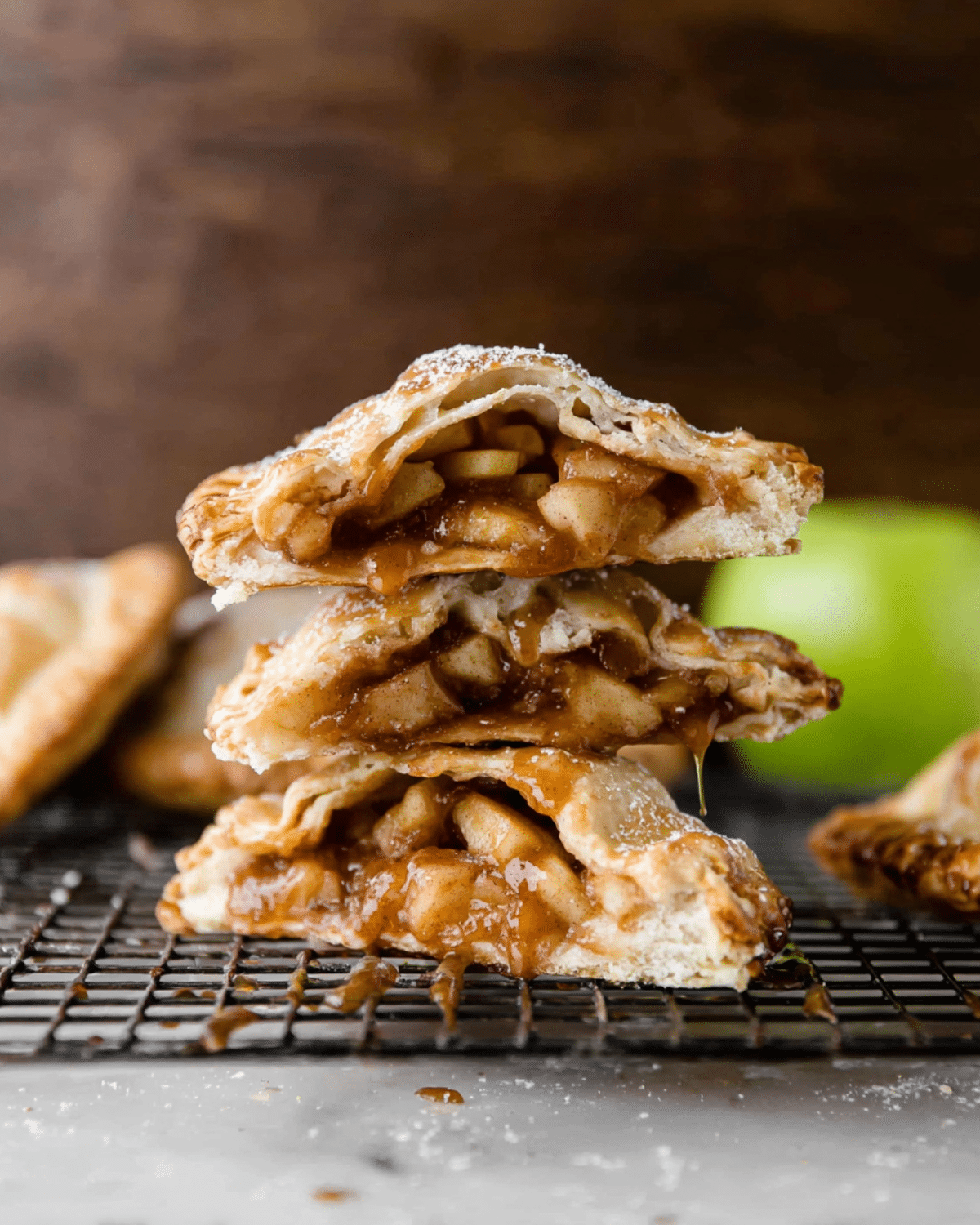 Apple hand pies with flaky crust stacked on a cooling rack, oozing warm caramelized apple filling.