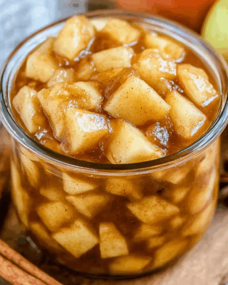 A close-up of a glass jar filled with apple pie filling, featuring tender apple chunks coated in cinnamon-spiced syrup.