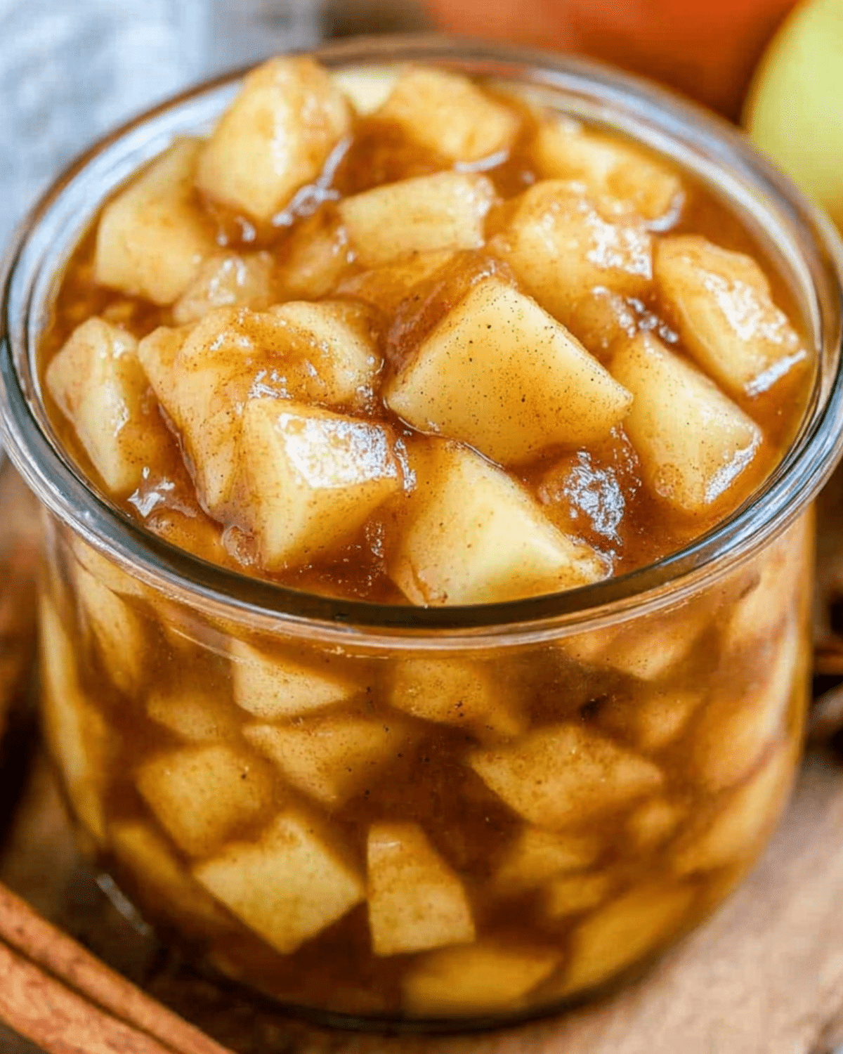A close-up of a glass jar filled with apple pie filling, featuring tender apple chunks coated in cinnamon-spiced syrup.