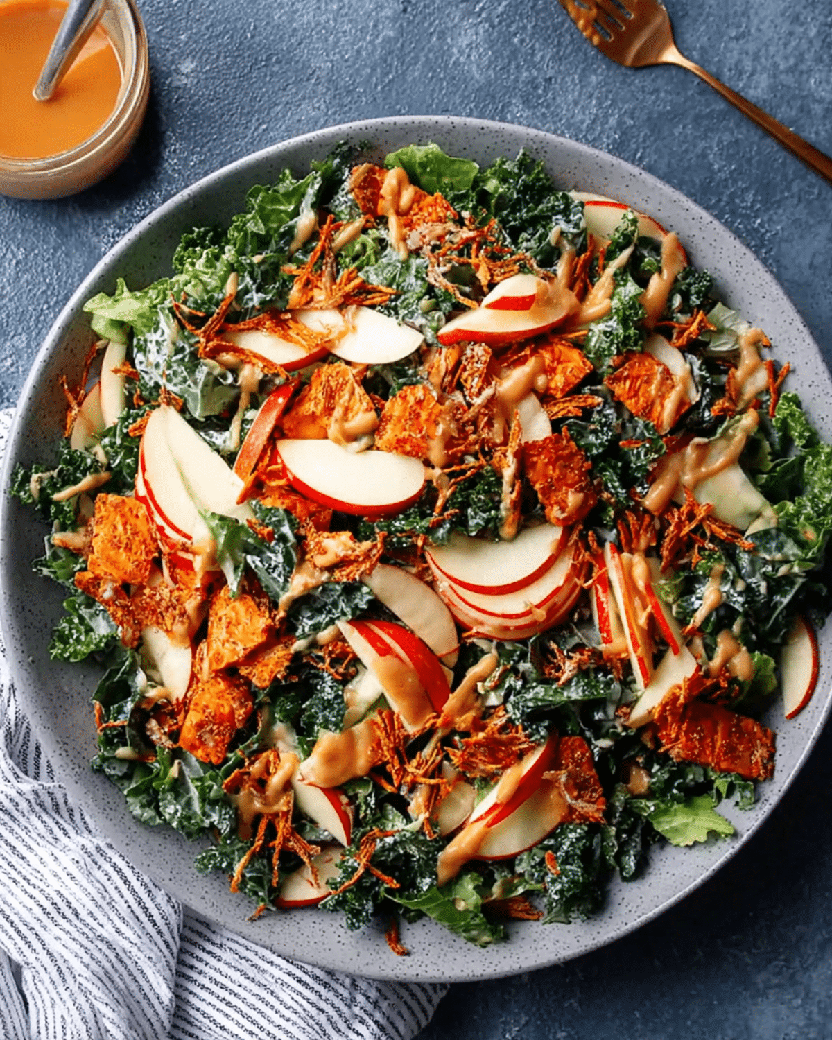 Fresh apple salad with cheddar, kale, and a drizzle of dressing served in a large gray bowl.
