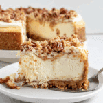Slice of autumn cheesecake topped with pecans and crumbly streusel on a white plate, with the rest of the cheesecake in the background.