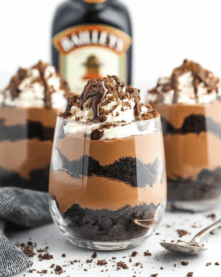 A glass filled with Baileys Chocolate Cheesecake Trifle layered with chocolate mousse, crushed cookies, whipped cream, and drizzled chocolate.