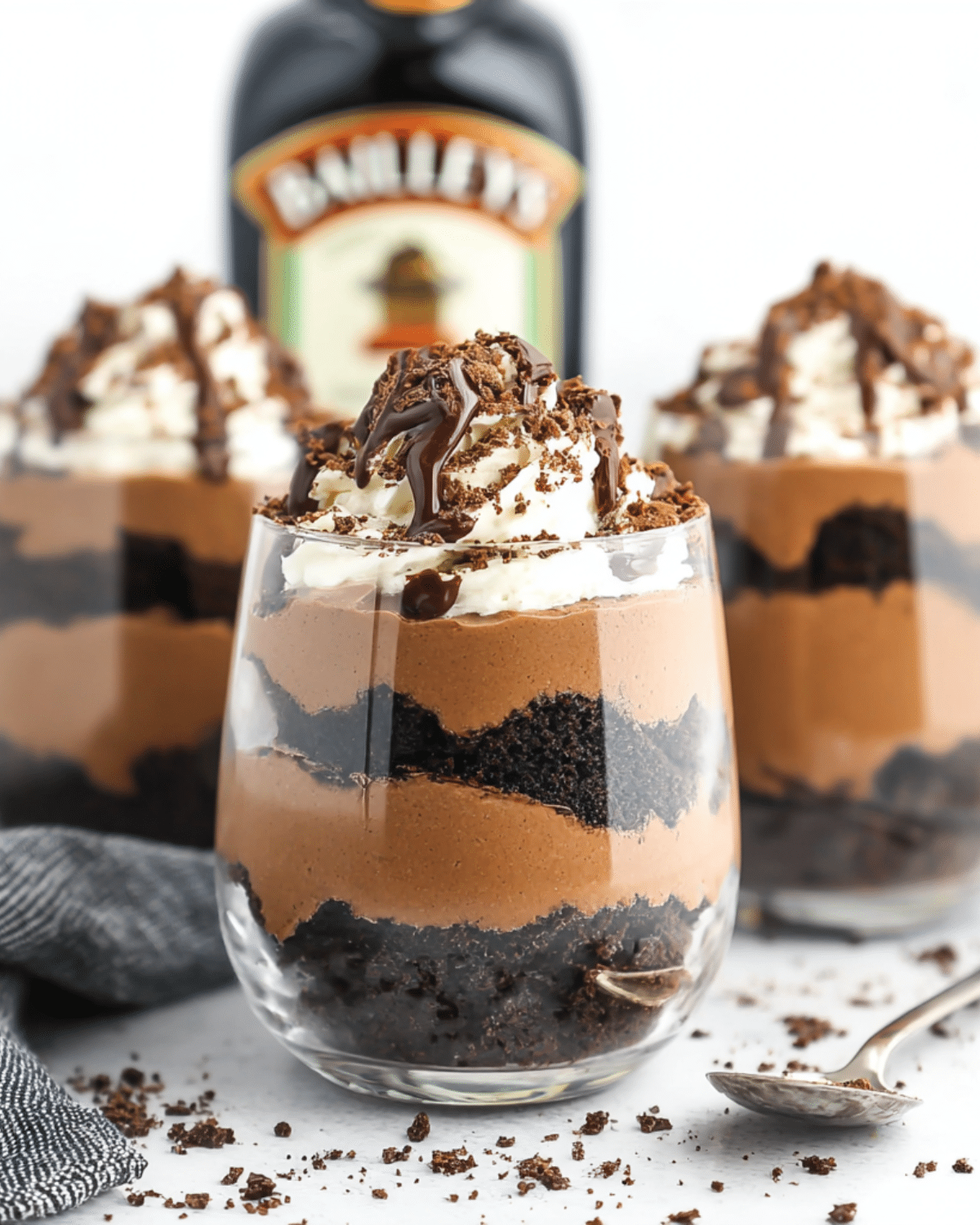 A glass filled with Baileys Chocolate Cheesecake Trifle layered with chocolate mousse, crushed cookies, whipped cream, and drizzled chocolate.