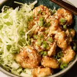 A bowl of Bang Bang Shrimp served with shredded cabbage, topped with sesame seeds and green onions.