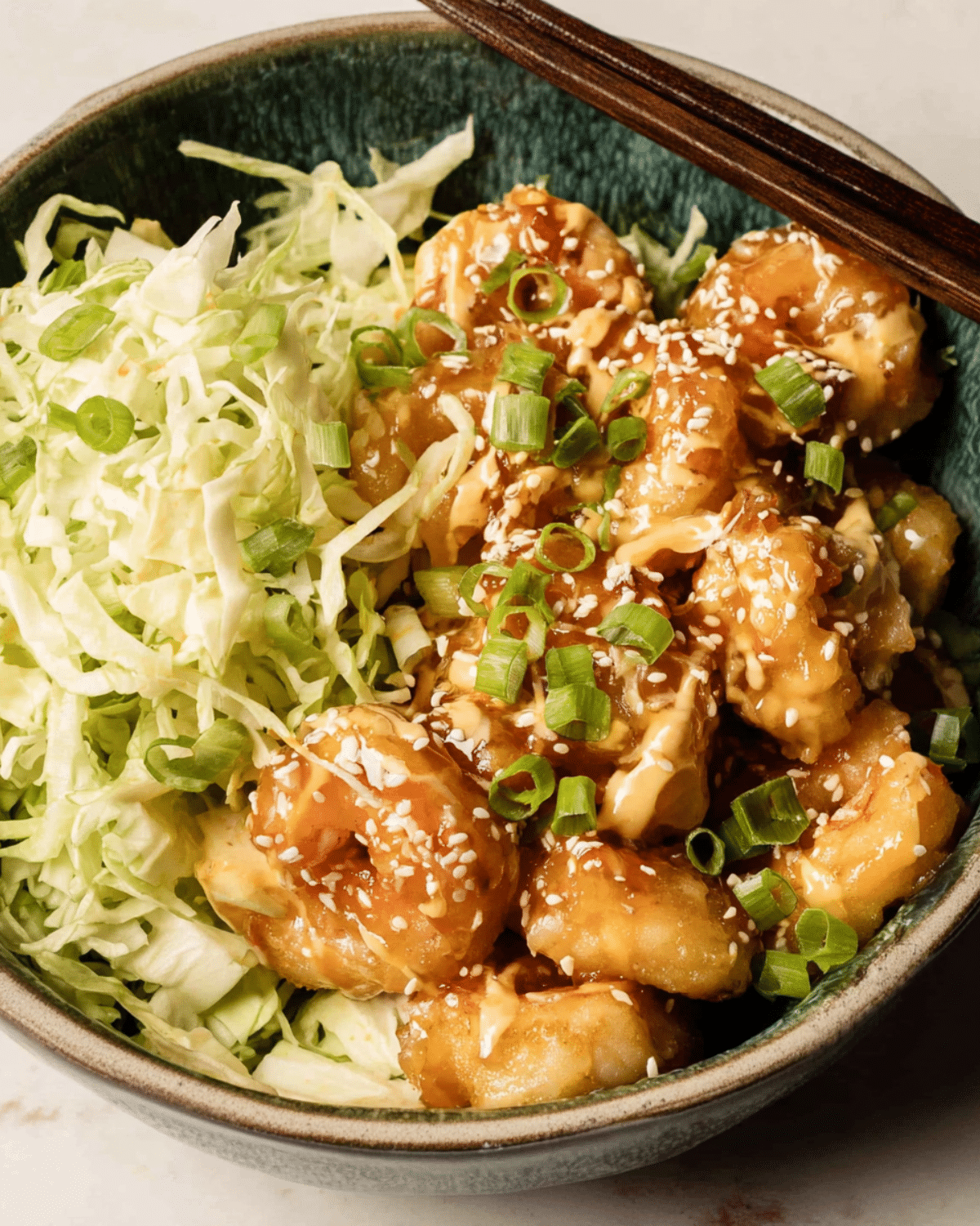 A bowl of Bang Bang Shrimp served with shredded cabbage, topped with sesame seeds and green onions.