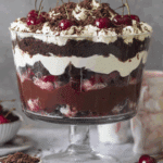 Layered Black Forest trifle in a glass dish with chocolate cake, cherries, whipped cream, and chocolate shavings.