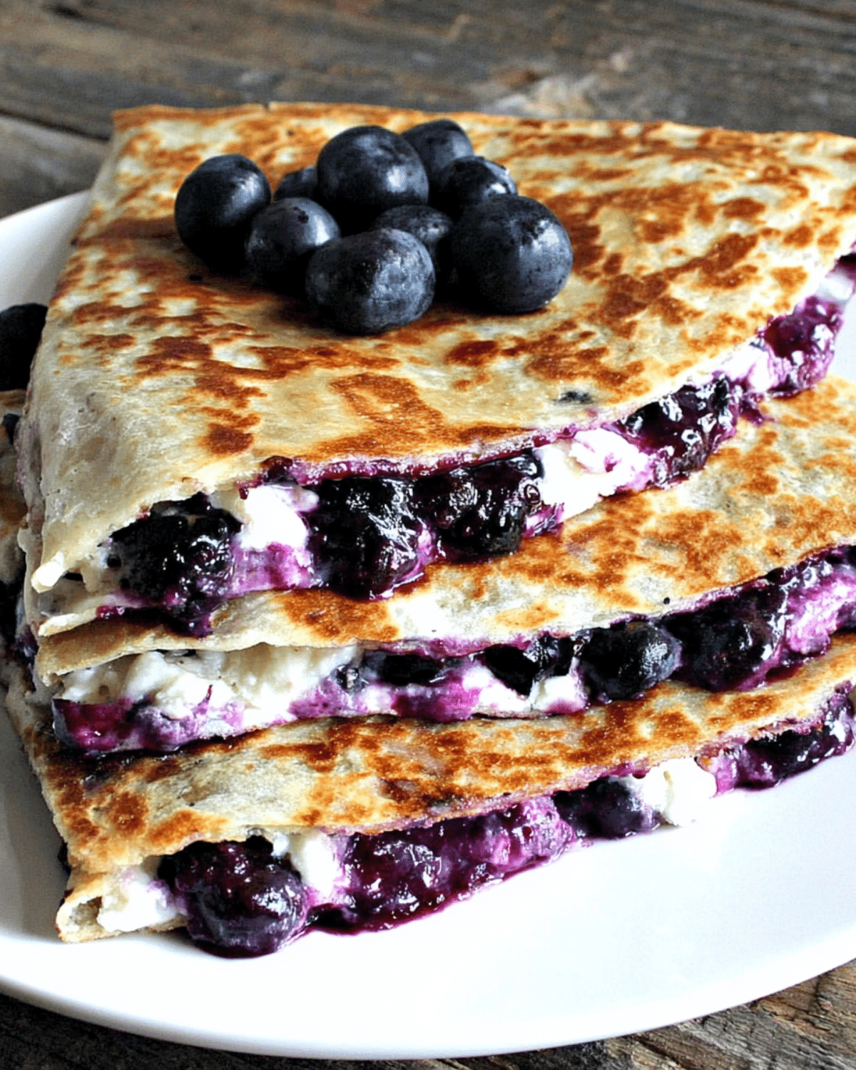 Blueberry breakfast quesadilla filled with fresh blueberries and creamy cheese, stacked on a white plate.