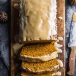 Sliced brown sugar pumpkin loaf with a thick glaze on top, served on a wooden cutting board.