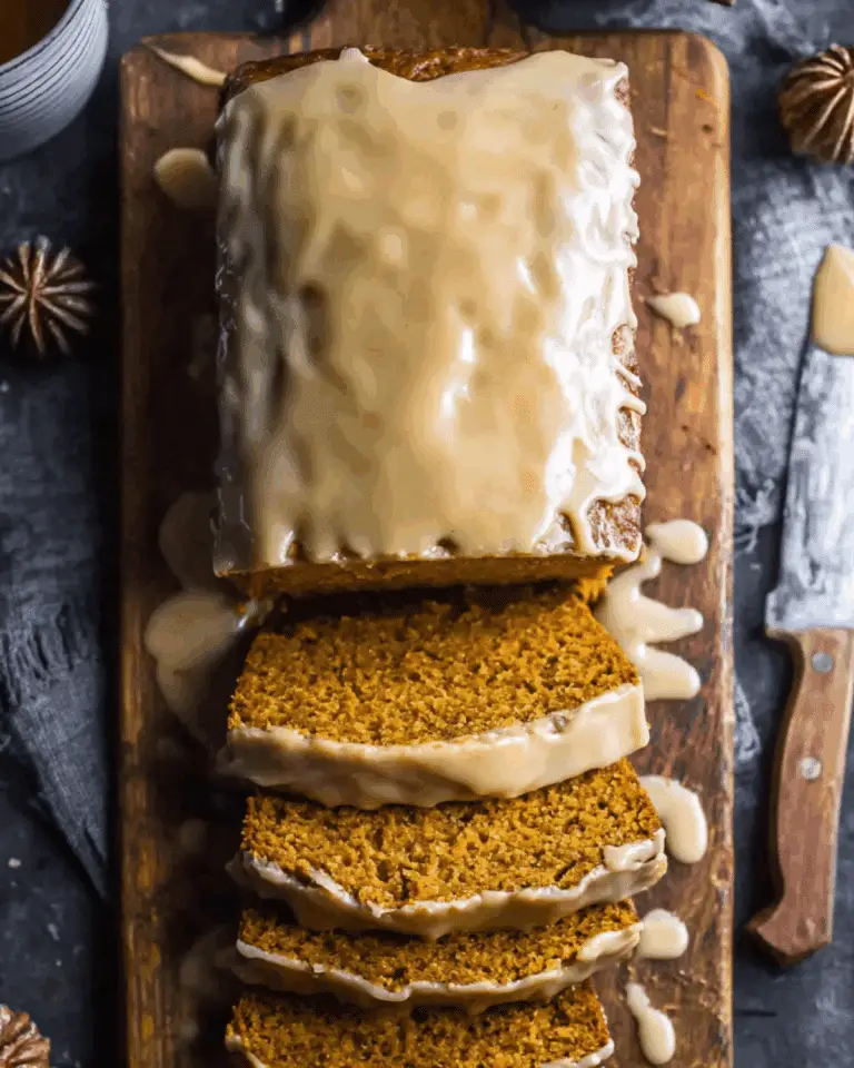 Sliced brown sugar pumpkin loaf with a thick glaze on top, served on a wooden cutting board.