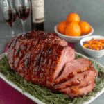 Brown Sugar Rum Baked Ham garnished with rosemary, served with wine, oranges, and side dishes.