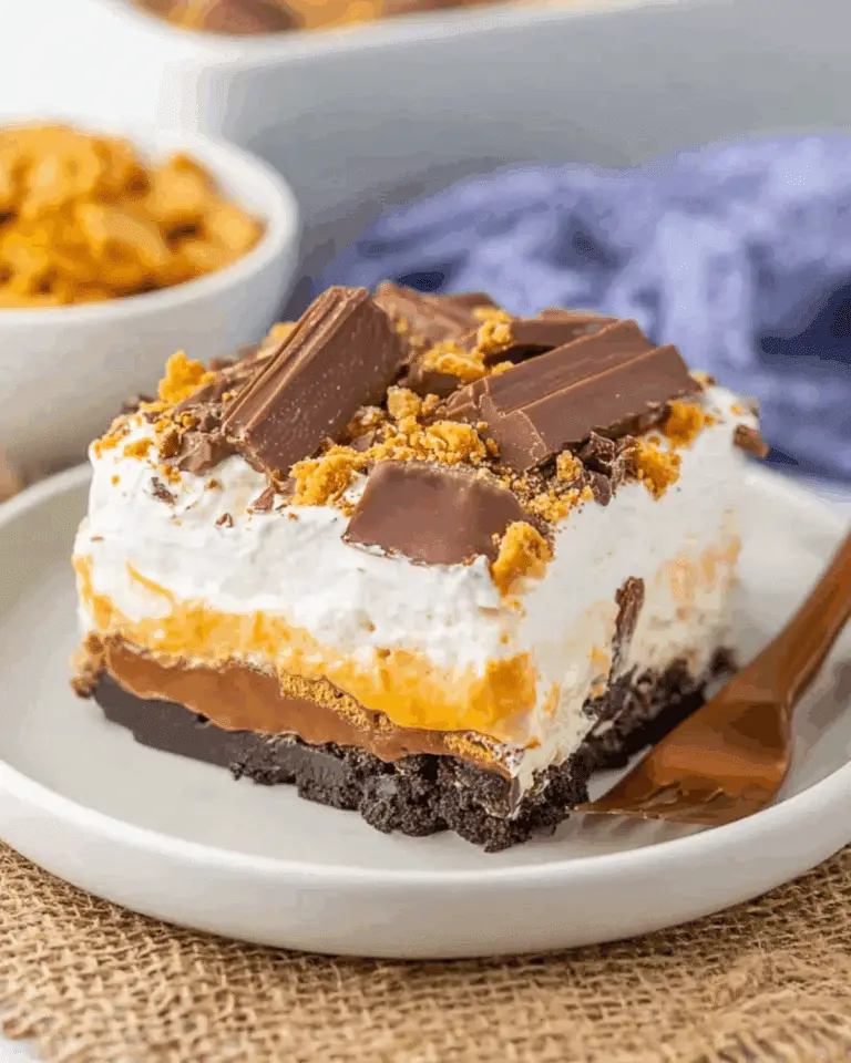 Slice of Butterfinger lush dessert on a white plate, featuring layers of whipped cream, chocolate, peanut butter, and crushed Butterfinger candy.