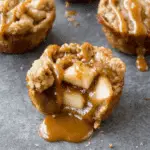 Caramel apple cup filled with cinnamon-spiced apple chunks, topped with streusel and drizzled with caramel sauce, with caramel oozing out.