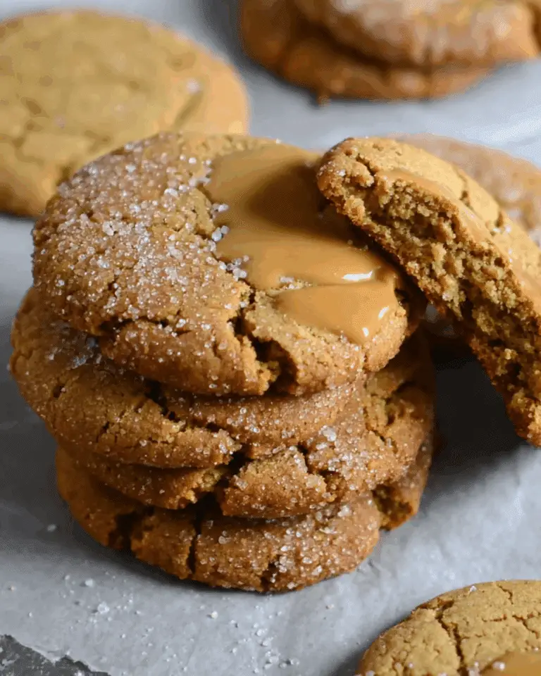 Stack of chewy pumpkin cookies topped with sugar and gooey caramel on parchment paper.