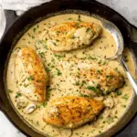 Chicken breast in white wine cream sauce garnished with fresh parsley, served in a cast-iron skillet.