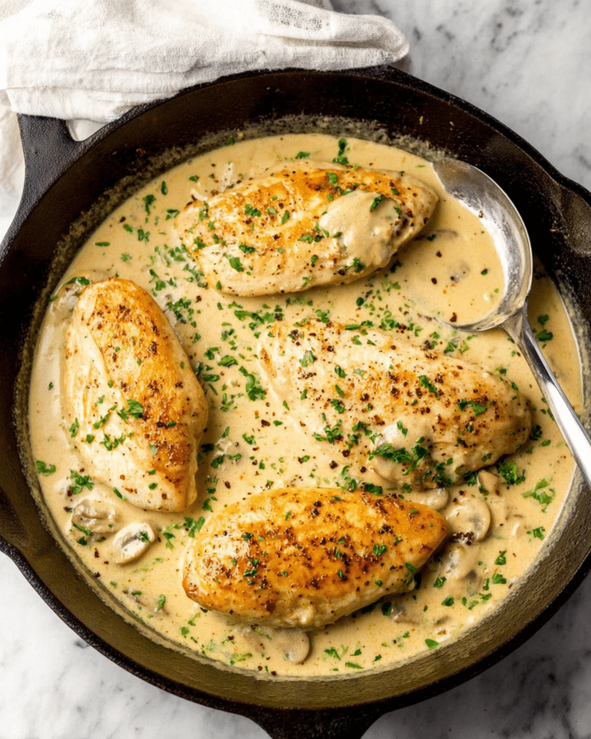 Chicken breast in white wine cream sauce garnished with fresh parsley, served in a cast-iron skillet.