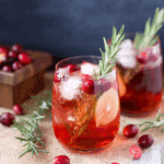 Christmas Apple Cranberry Spritzer in a glass with ice, fresh cranberries, apple slices, and rosemary garnish.