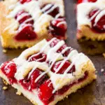 Christmas Cherry Bars with a golden crust, cherry filling, and white icing drizzle cut into squares.