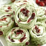 Christmas Cranberry Roll Ups made with spinach tortillas, cream cheese, and dried cranberries on a white platter.