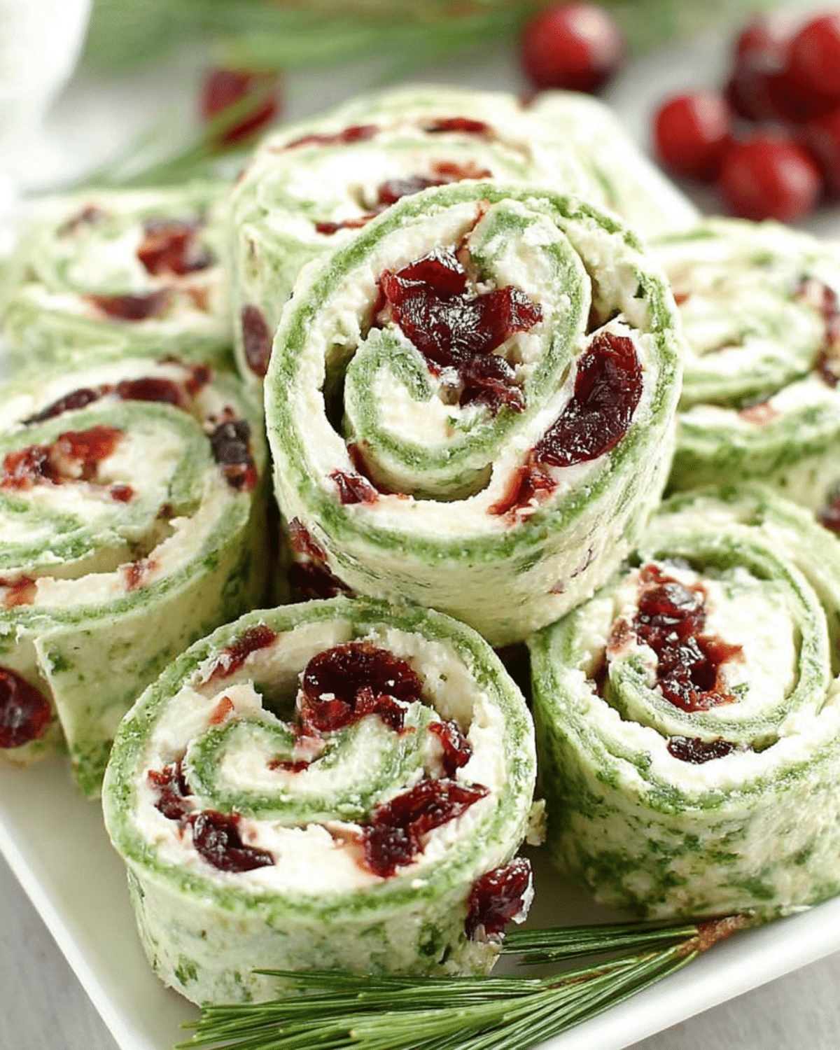 Christmas Cranberry Roll Ups made with spinach tortillas, cream cheese, and dried cranberries on a white platter.