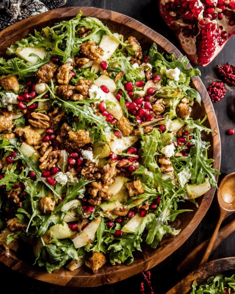 Wooden bowl filled with Christmas salad featuring arugula, pomegranate seeds, sliced pears, candied pecans, croutons, and crumbled cheese, drizzled with honey mustard dressing.
