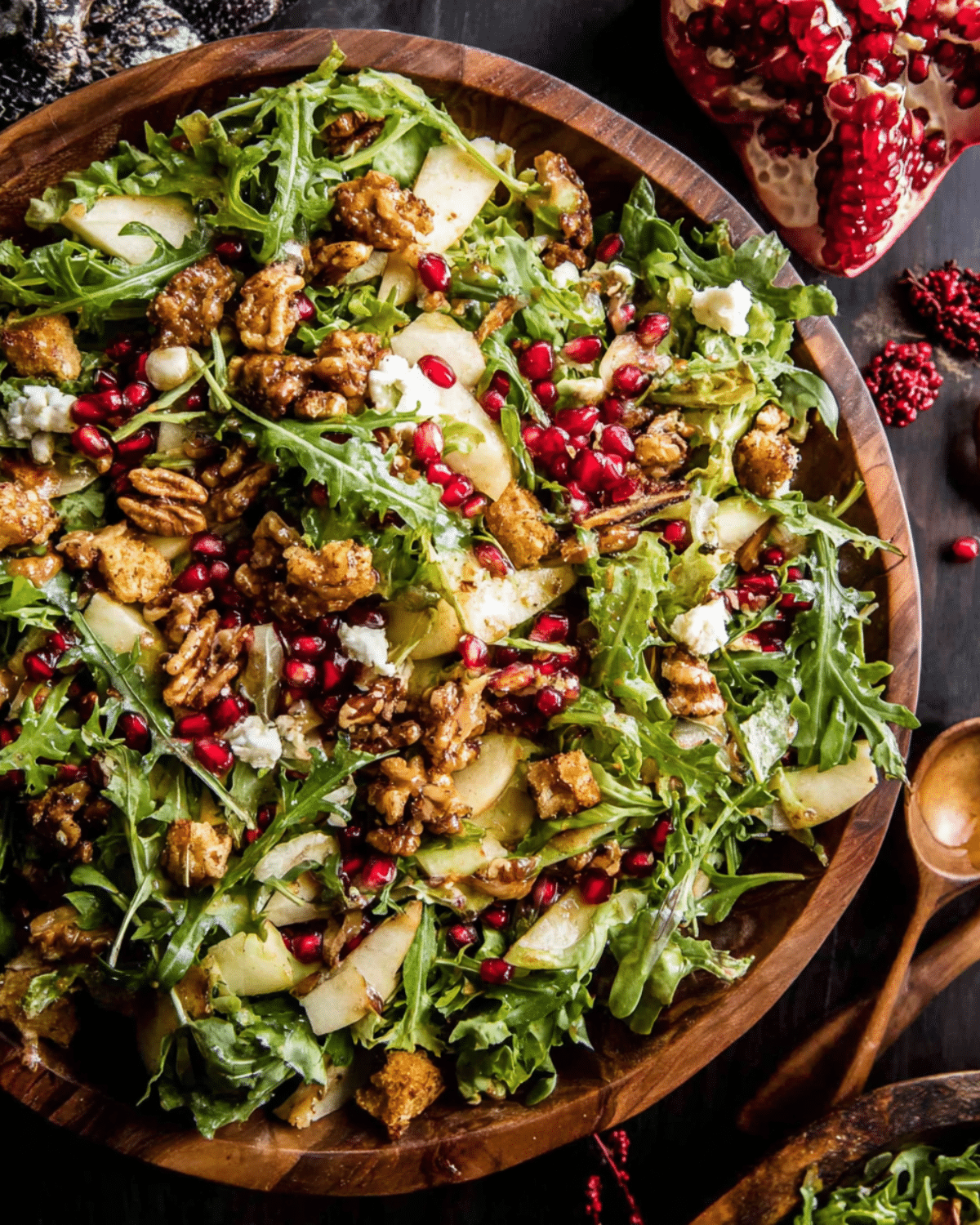 Wooden bowl filled with Christmas salad featuring arugula, pomegranate seeds, sliced pears, candied pecans, croutons, and crumbled cheese, drizzled with honey mustard dressing.