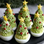Christmas Tree Deviled Eggs decorated with green avocado filling, red garnish, and cheese stars on top.
