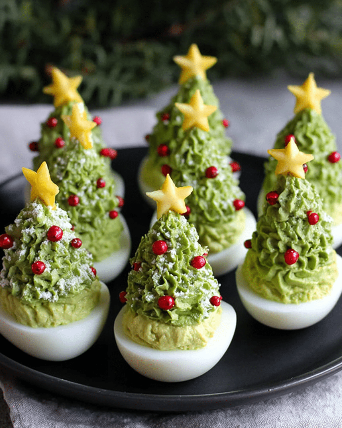 Christmas Tree Deviled Eggs decorated with green avocado filling, red garnish, and cheese stars on top.