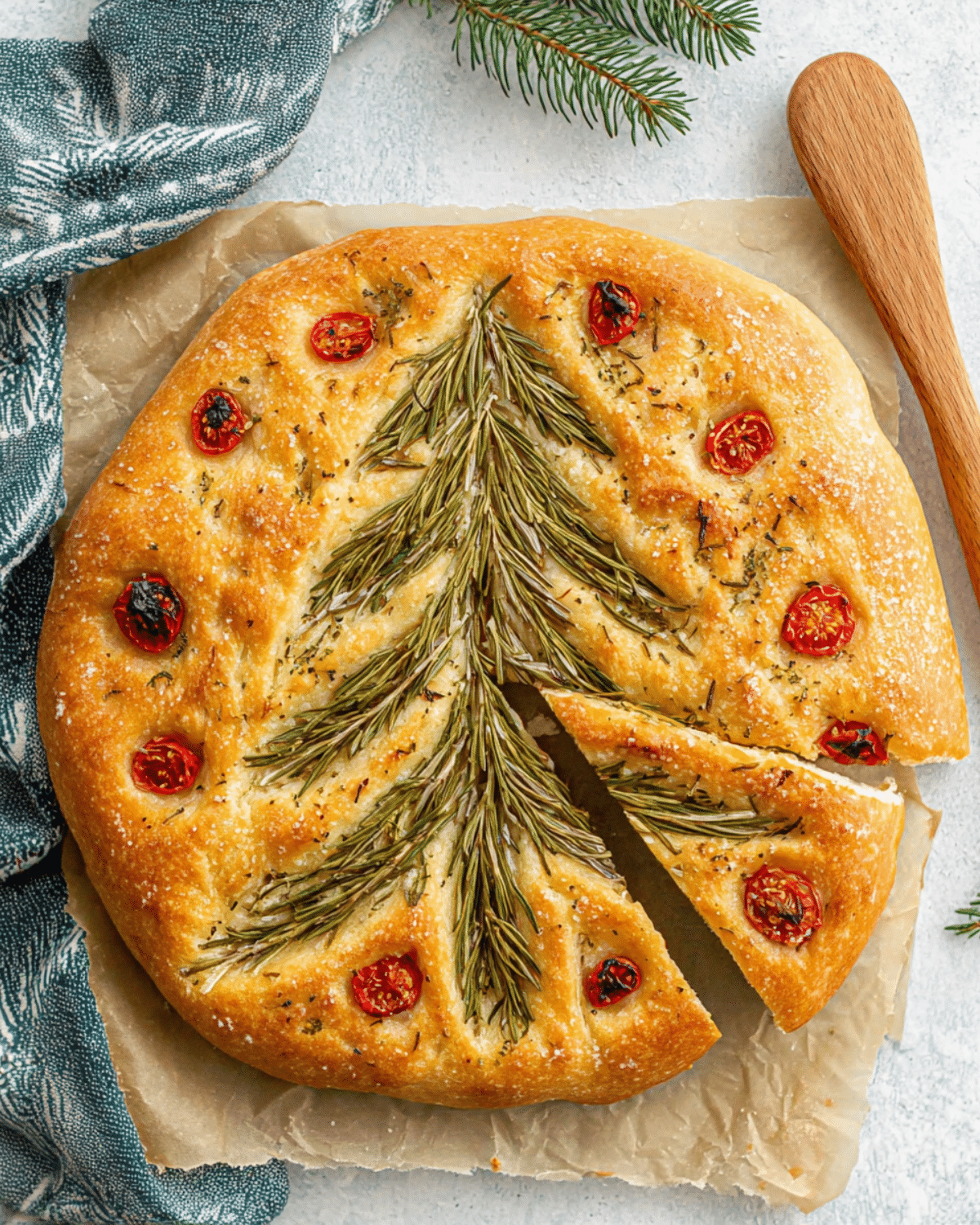 Round focaccia bread decorated with rosemary sprigs arranged as a Christmas tree and cherry tomato ornaments.