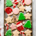 A tray of decorated Christmas sugar cookies in festive shapes like trees, candy canes, snowflakes, and Santa hats.