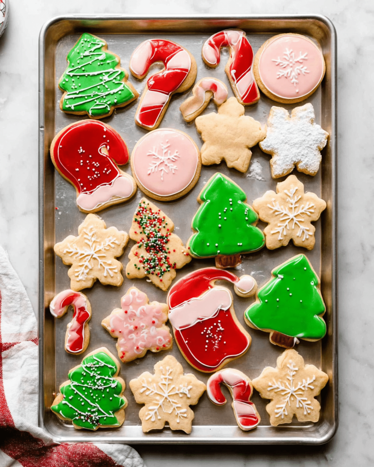A tray of decorated Christmas sugar cookies in festive shapes like trees, candy canes, snowflakes, and Santa hats.
