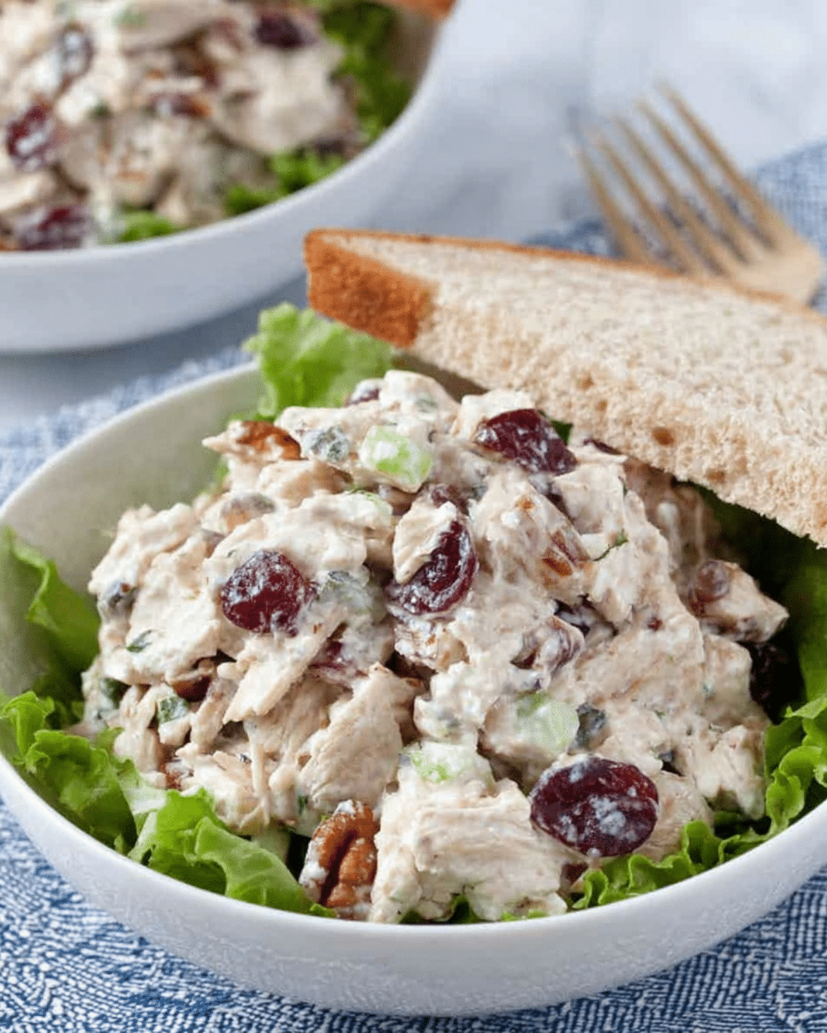 Bowl of cranberry pecan chicken salad with lettuce, served with a slice of bread on the side.