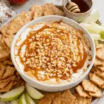 Cream cheese caramel apple dip topped with chopped nuts and caramel sauce, served with crackers and green apple slices.