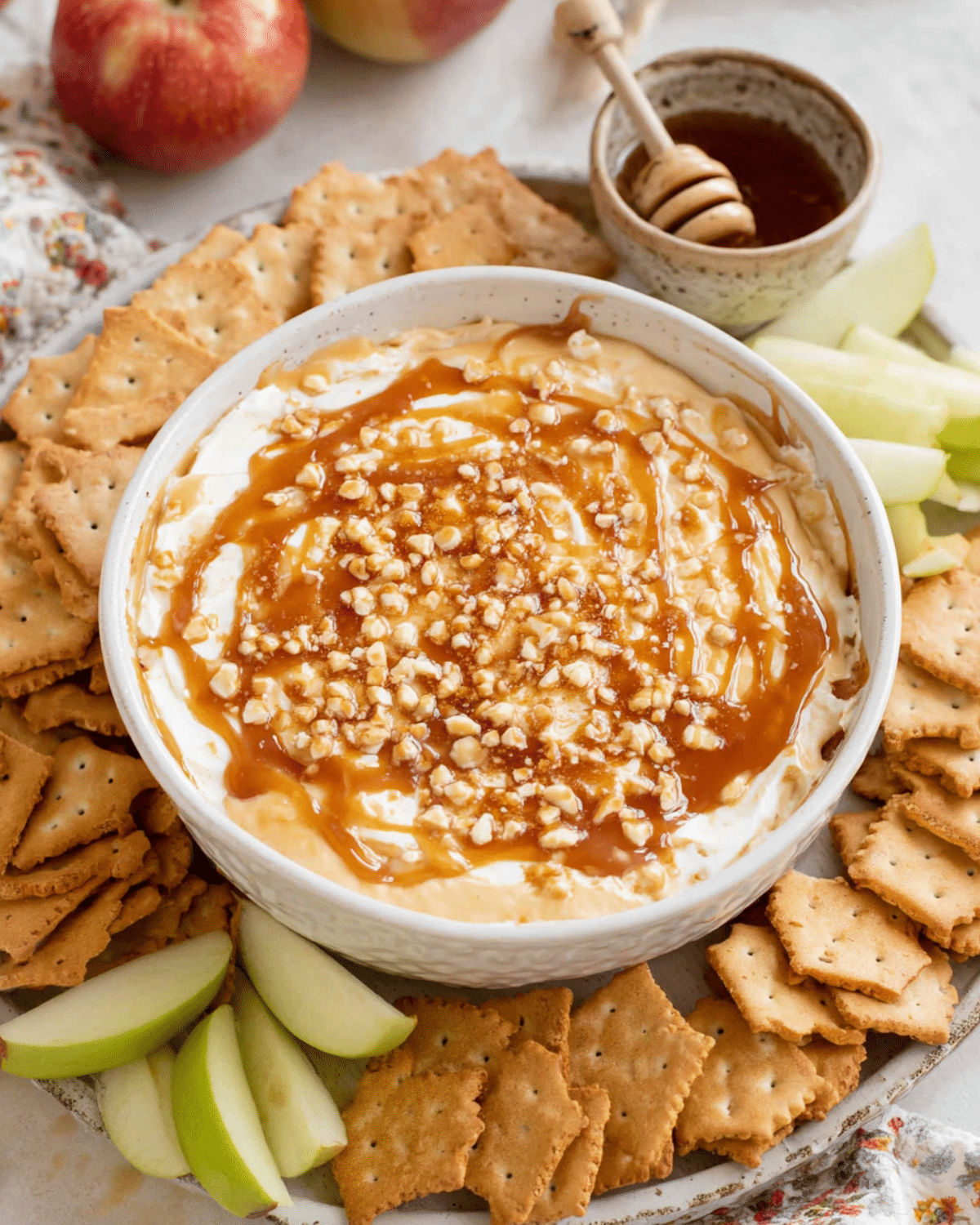 Cream cheese caramel apple dip topped with chopped nuts and caramel sauce, served with crackers and green apple slices.