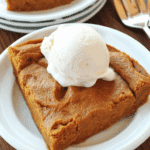 A slice of crustless pumpkin pie topped with a scoop of vanilla ice cream on a white plate.
