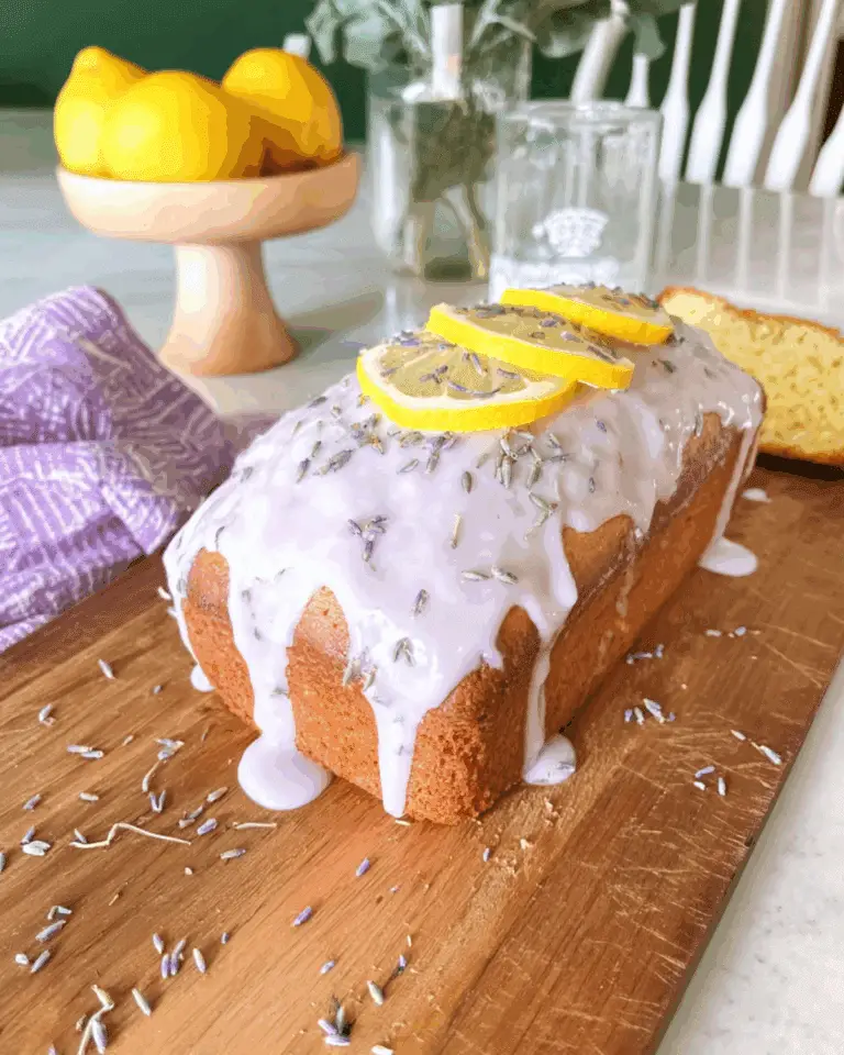 Delicious lemon lavender loaf topped with glaze, lemon slices, and dried lavender on a wooden board.