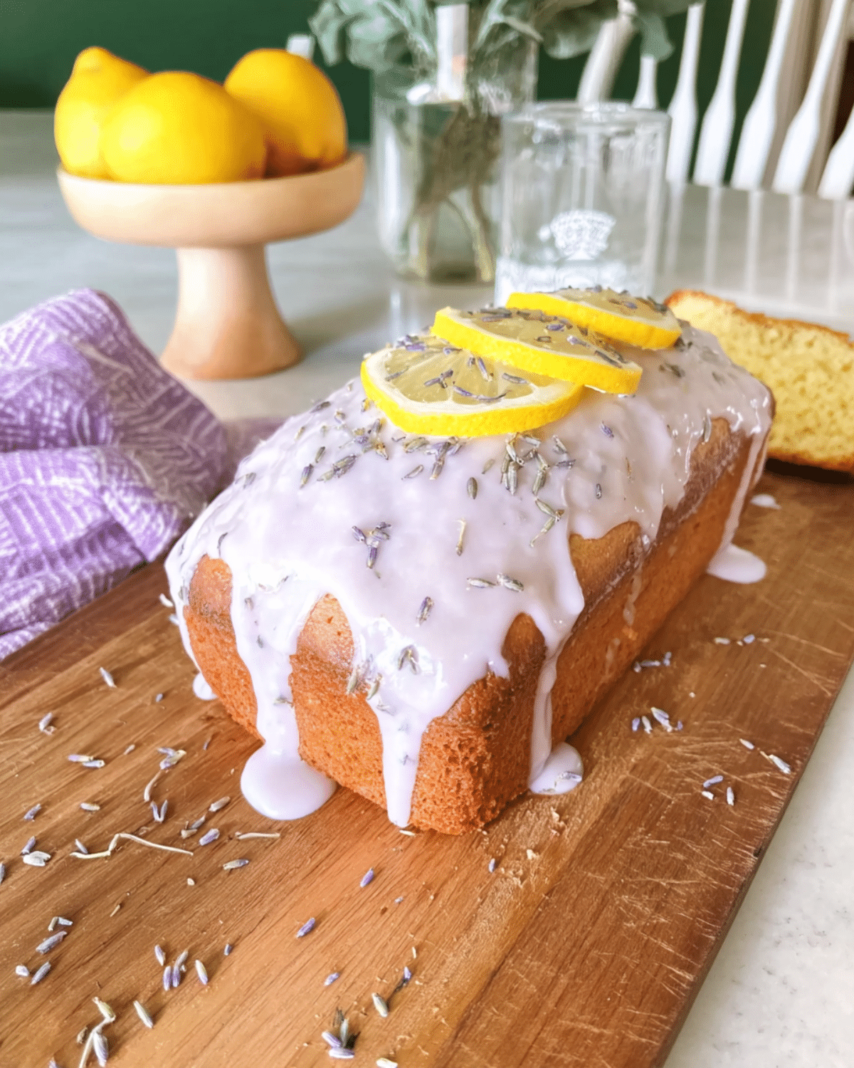 Delicious lemon lavender loaf topped with glaze, lemon slices, and dried lavender on a wooden board.