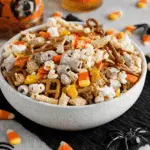 White bowl filled with easy Halloween snack mix including popcorn, pretzels, Chex cereal, candy corn, and festive treats.