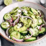 A bowl of Easy Mexican Cucumber Salad with avocado, red onion, crumbled feta, and herbs.
