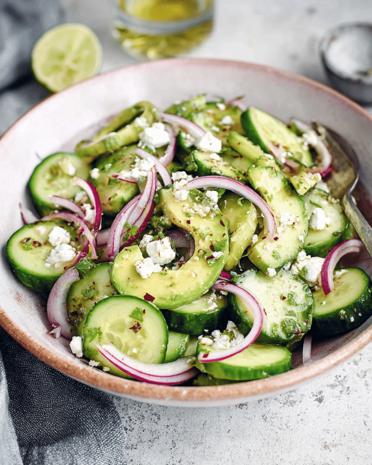 A bowl of Easy Mexican Cucumber Salad with avocado, red onion, crumbled feta, and herbs.