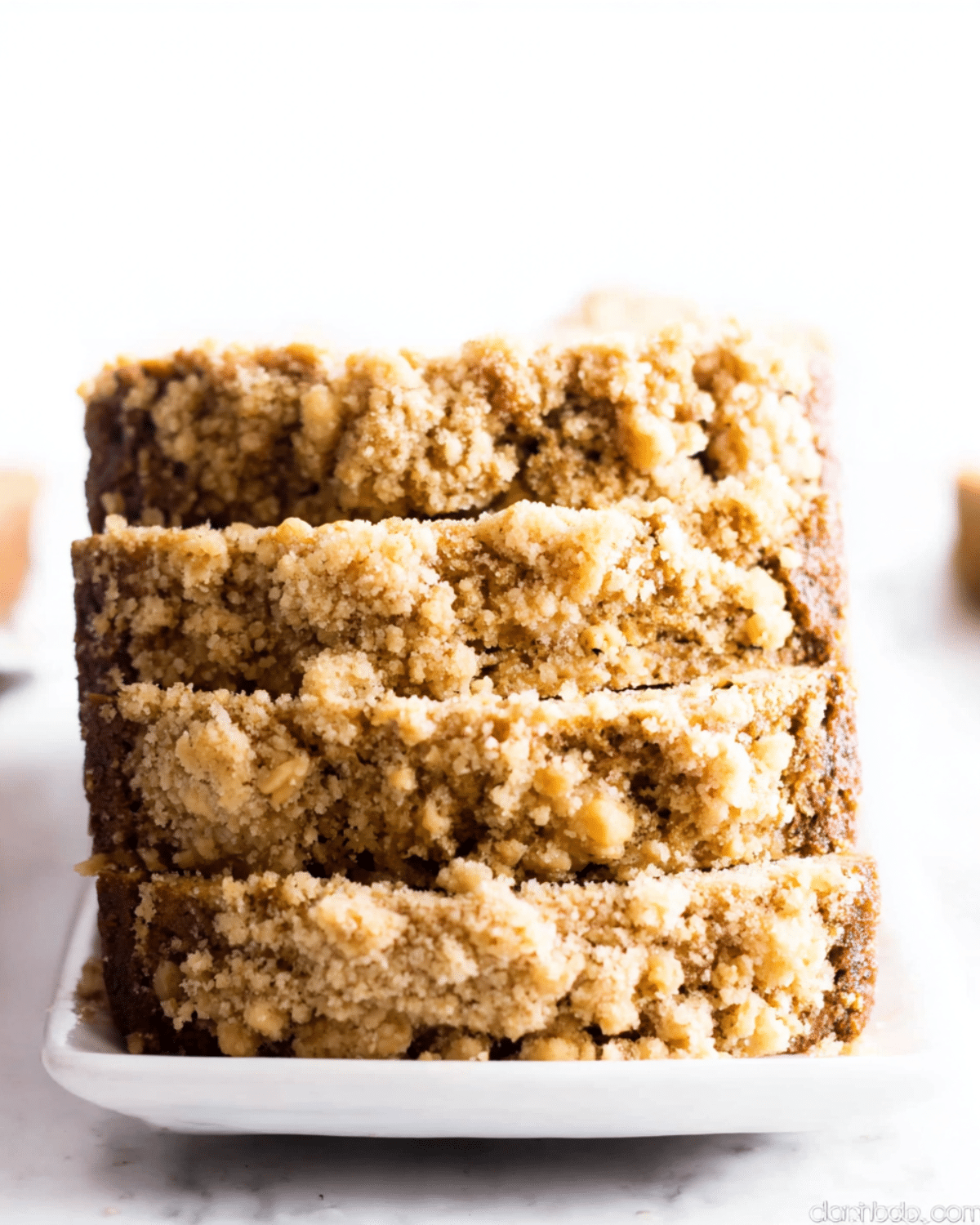 Easy pumpkin bread recipe with sweet crumb topping, sliced and stacked on a white rectangular plate.