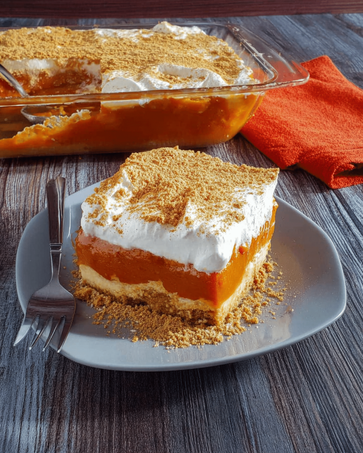 A slice of easy pumpkin delight topped with whipped cream and graham cracker crumbs, served on a gray plate.