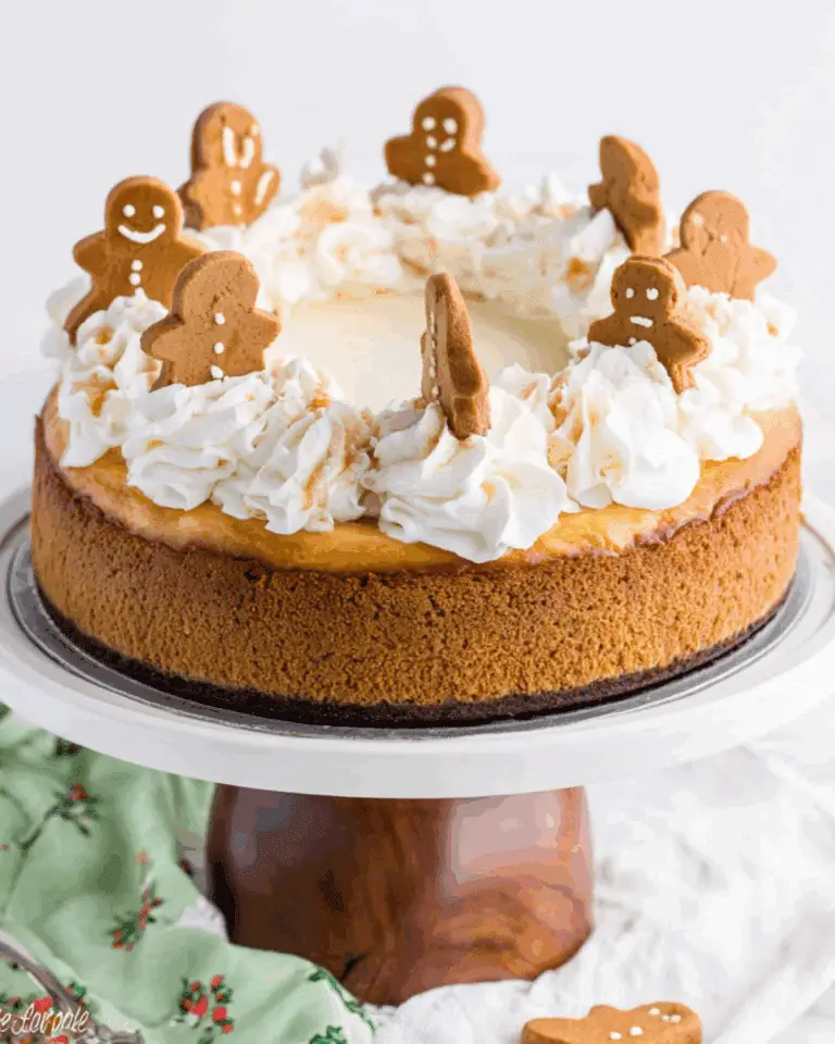 Gingerbread Cheesecake Cake topped with whipped cream swirls and decorated with mini gingerbread cookies on a cake stand.